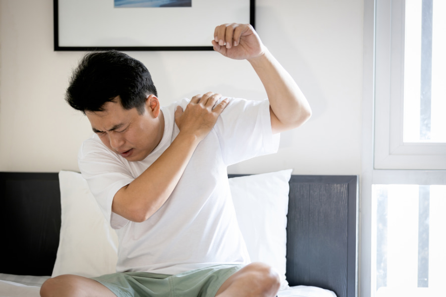 man feeling neck and shoulder pain and testing his arm's range of motion