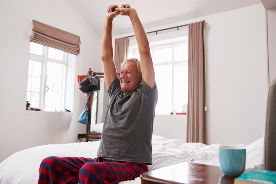 image of a senior man sitting on a bed and stretching his back and arms